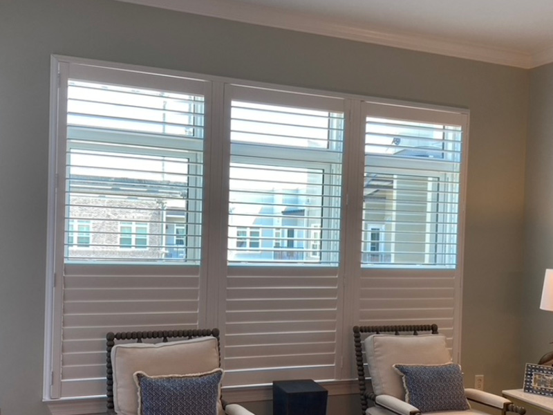 The image shows a room with white vertical blinds covering large windows, and there is a view of an outdoor area through the glass.