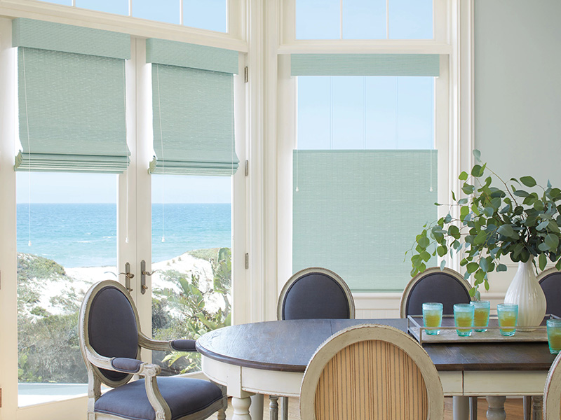 The image shows an interior view of a dining area with a large window offering a view of the ocean, and the room is furnished with chairs and a table.